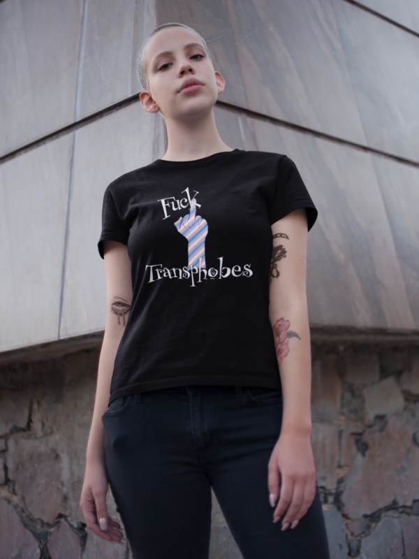 shaved head punk woman with trans flag color design on shirt that says fuck transphobes